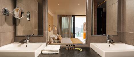 A modern bathroom with two sinks, a large mirror, and a view of a bedroom with a balcony.