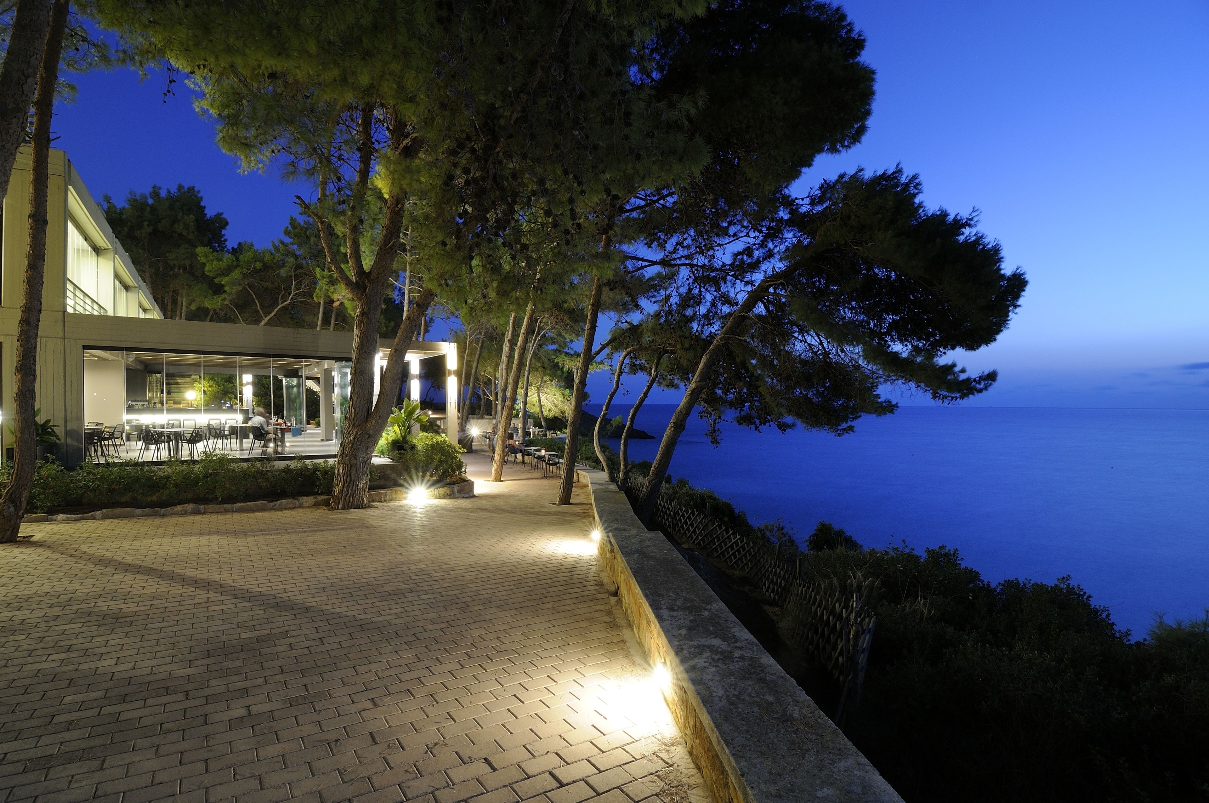 Un sendero pavimentado con mesas al aire libre, con vista a una masa de agua al anochecer.