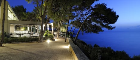 A paved walkway with outdoor seating, overlooking a body of water at dusk.