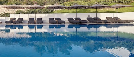 A pool area with lounge chairs and umbrellas, surrounded by a stone wall and greenery.