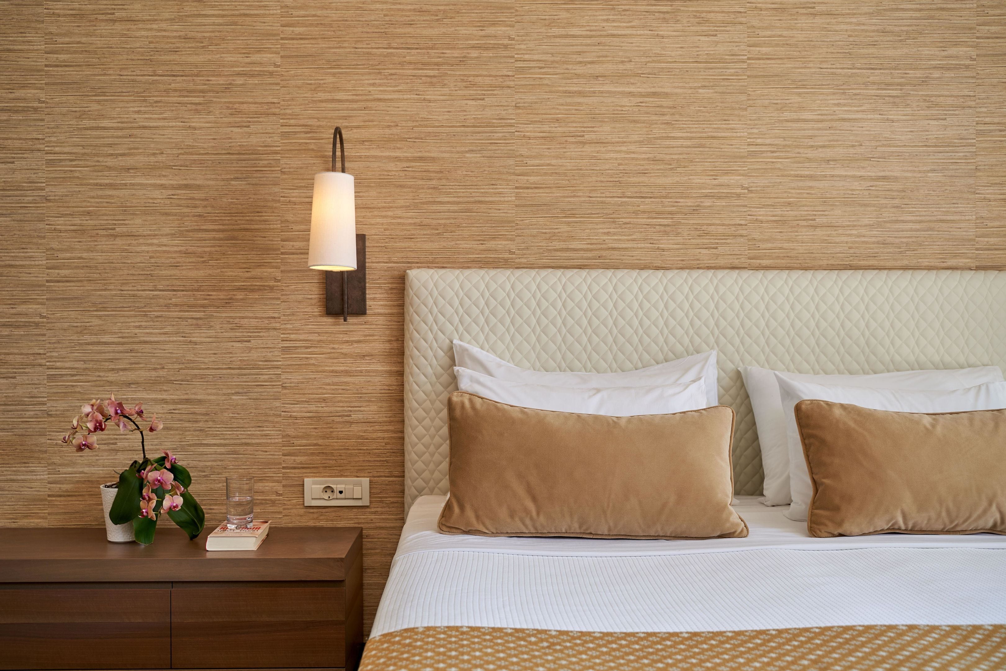 A neatly made bed with a quilted headboard, a bedside table with a lamp, and a potted orchid.