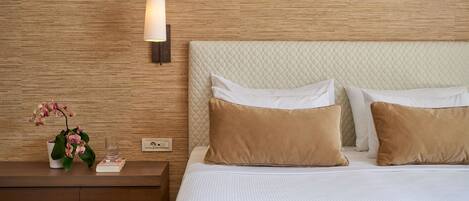 A neatly made bed with a quilted headboard, a bedside table with a lamp, and a potted orchid.