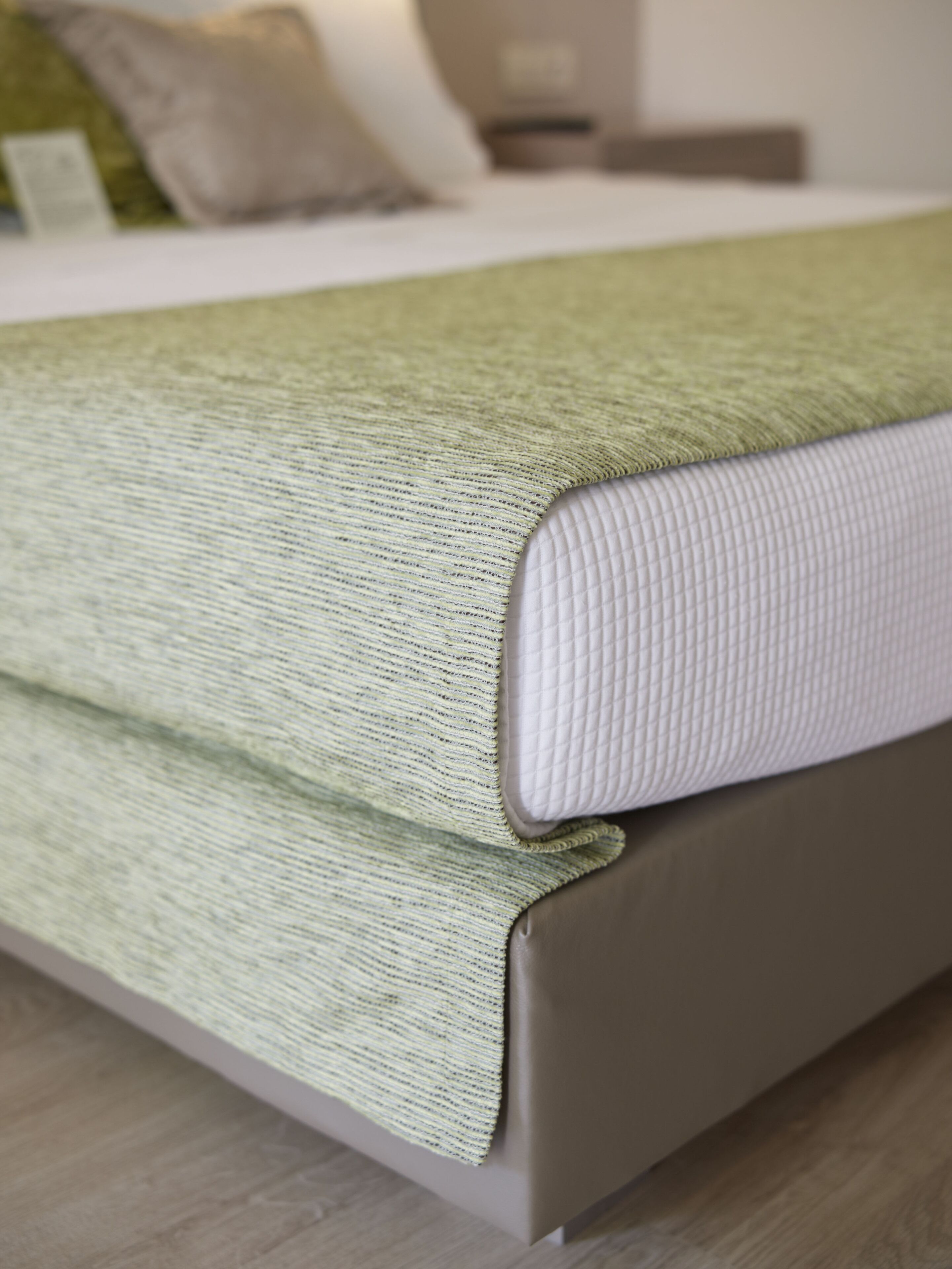 A bed with a green and white textured blanket, a white pillow, and a wooden headboard.