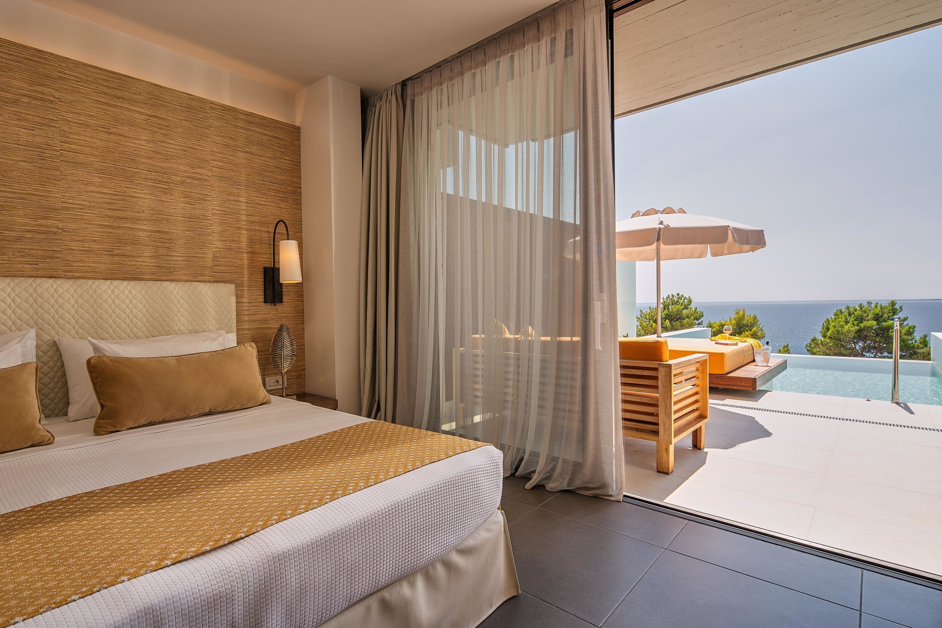 Ein Schlafzimmer mit großem Bett, Meerblick und einem Balkon mit Pool und Sitzgelegenheit im Freien.