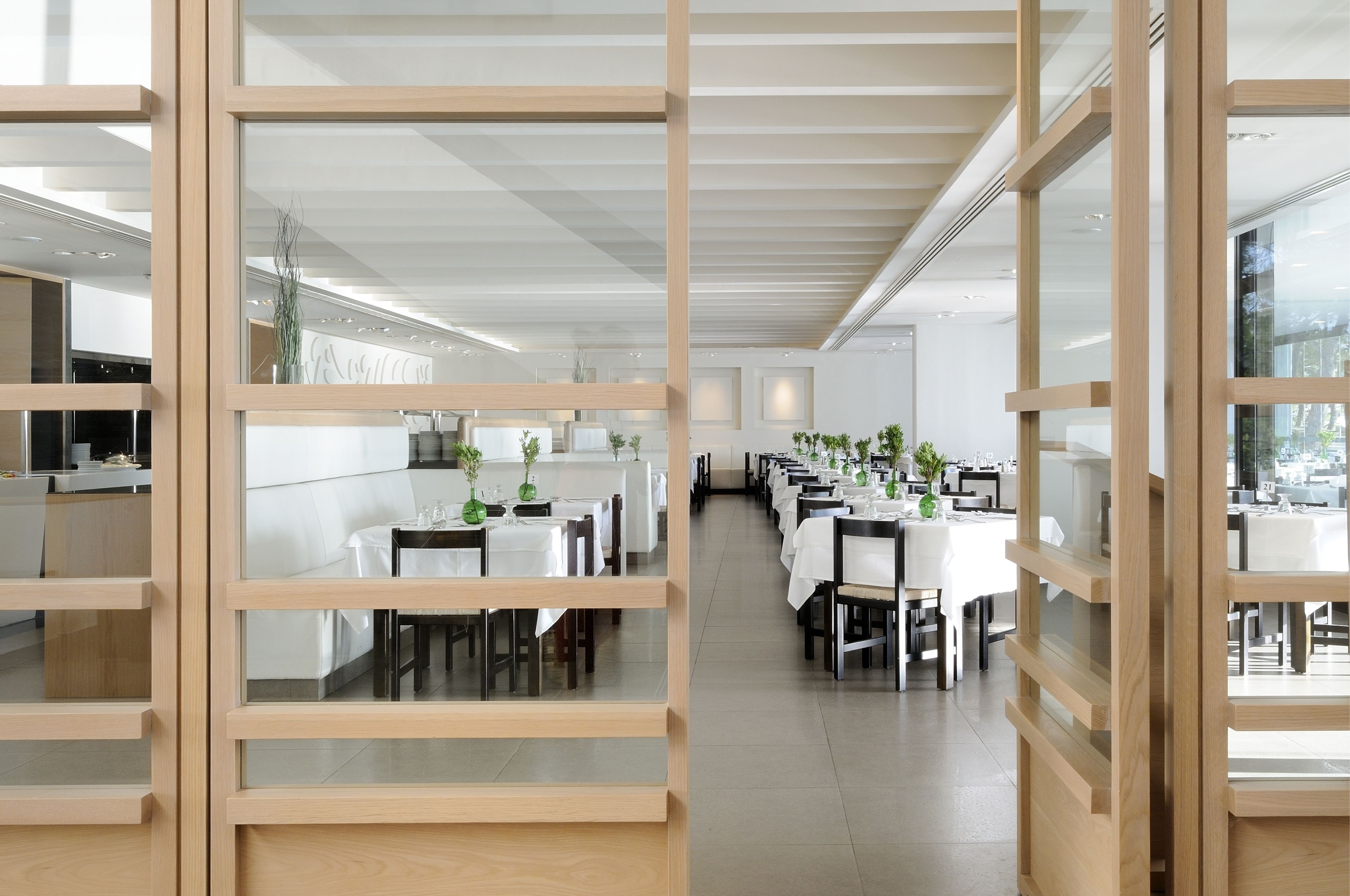 A modern dining area with white tables and chairs, wooden partitions, and potted plants.