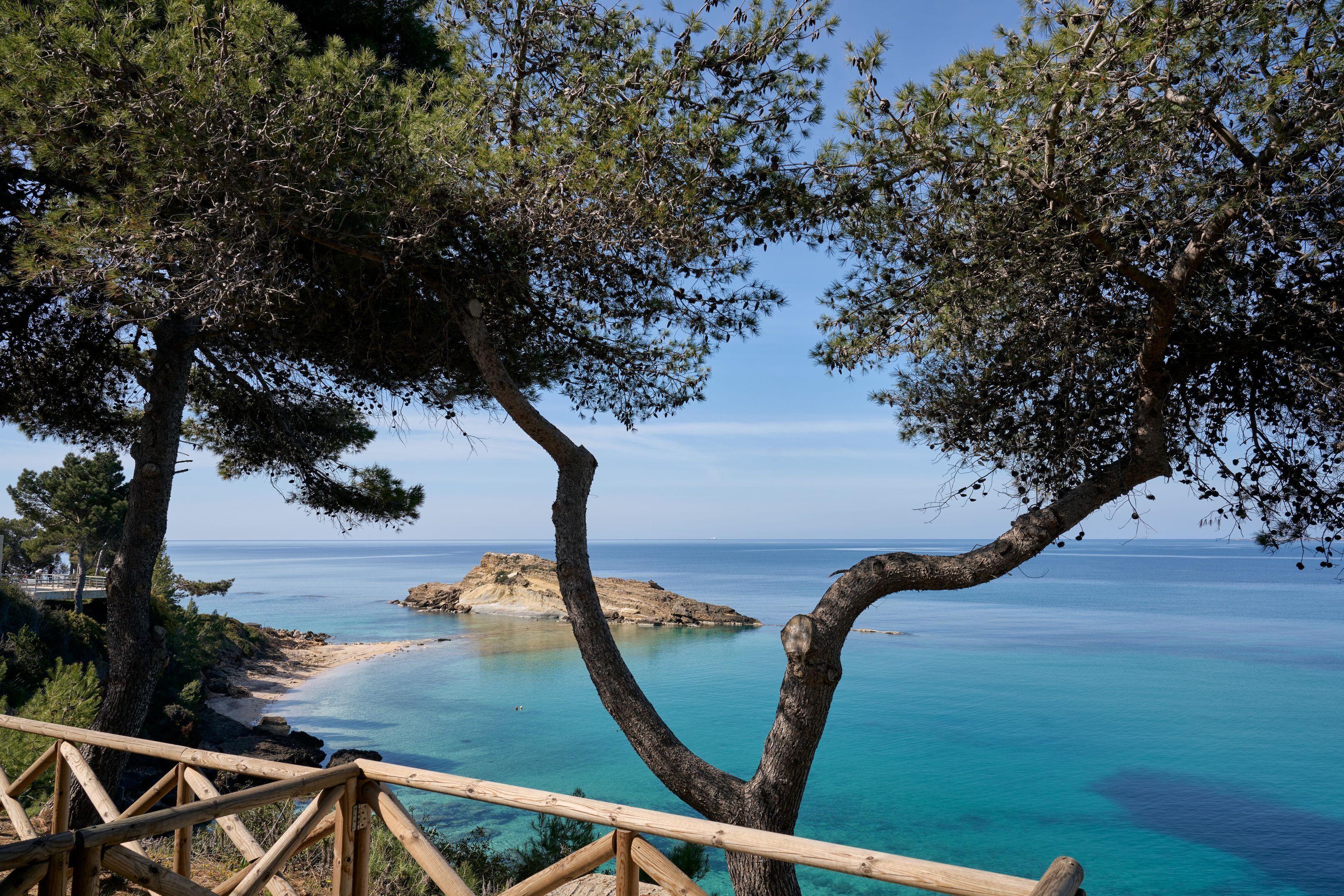 A coastal view with a wooden deck overlooking turquoise waters and a sandy beach.