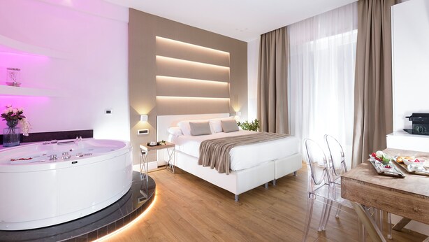 A modern bedroom with a large bed, a built-in bathtub, and a dining area with clear chairs.
