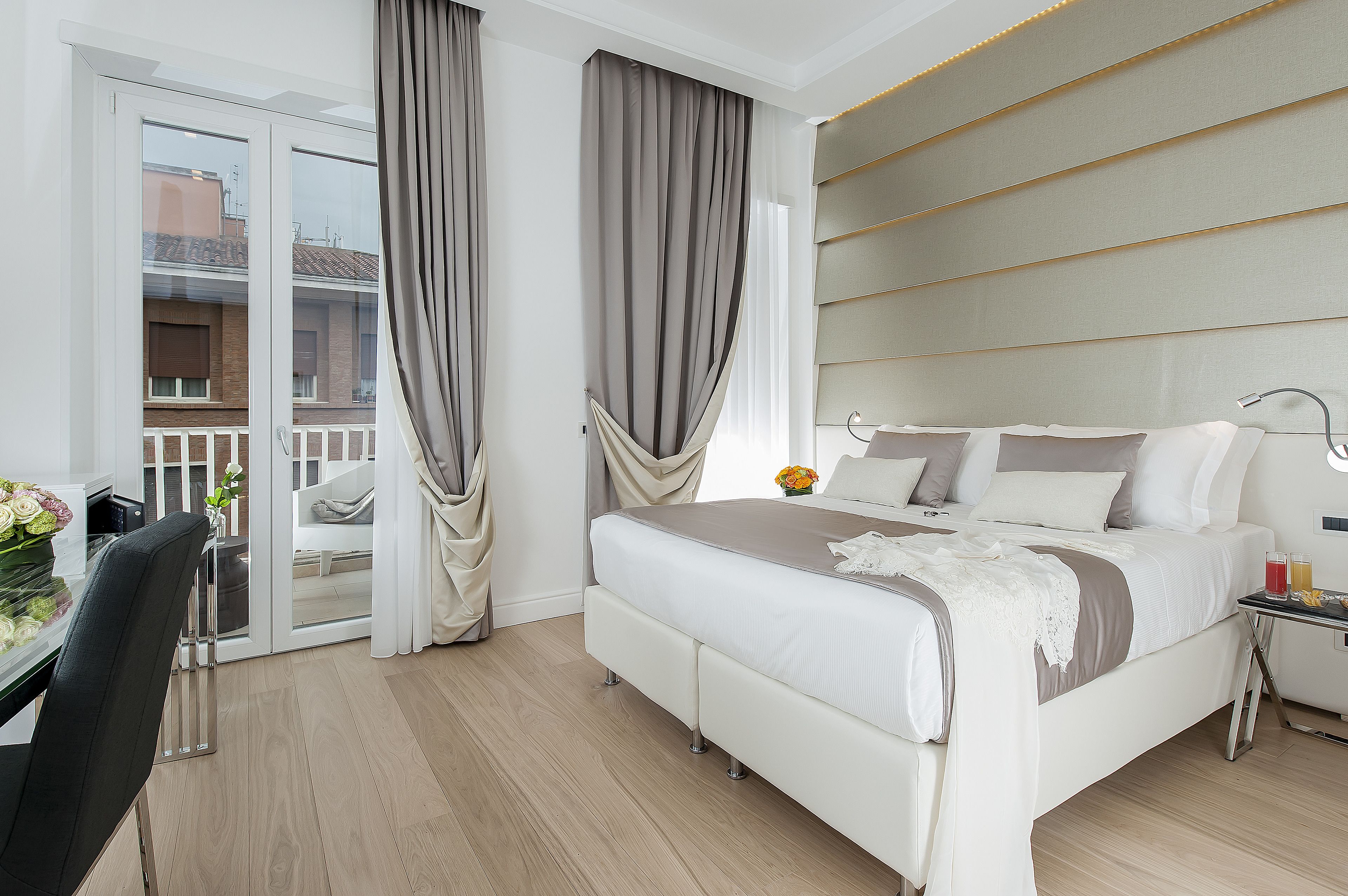 A modern hotel room with a bed, bedside table, and a view of the outside balcony.