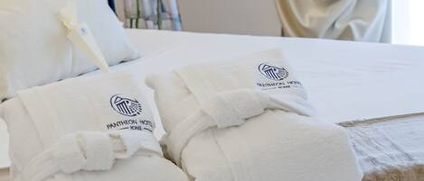 Two neatly folded white towels with the Pantheon Hotel logo on a bed.