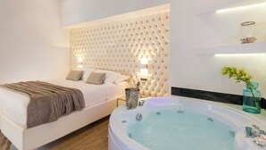 A modern bedroom with a large bed, a built-in headboard, a bedside table with a lamp, and a large bathtub.