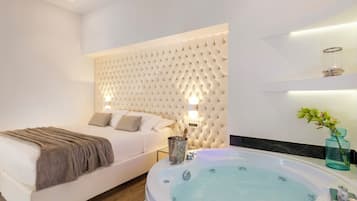 A modern bedroom with a large bed, a built-in headboard, a bedside table with a lamp, and a large bathtub.