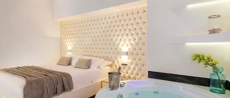 Un dormitorio moderno con una cama grande, cabecera integrada, mesita de noche con lámpara y una bañera espaciosa.