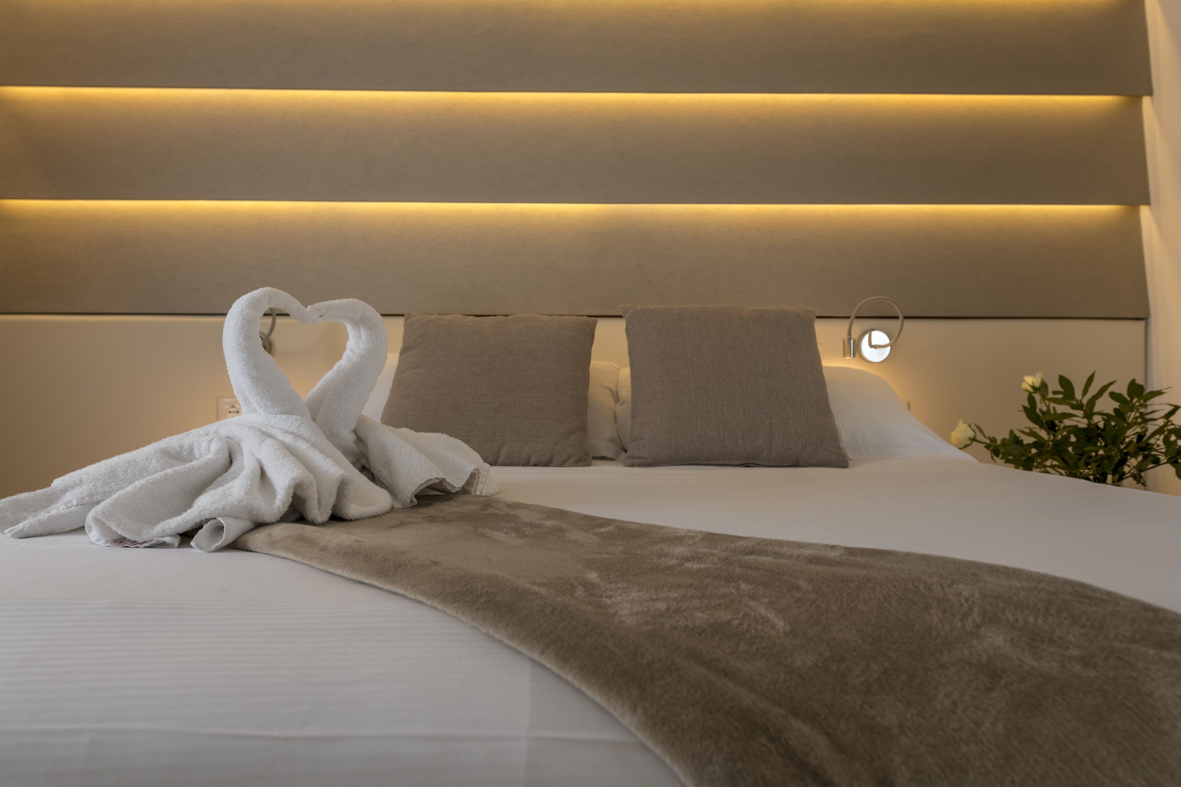 A neatly made bed with a heart-shaped towel arrangement, a fluffy throw blanket, and a bedside lamp.