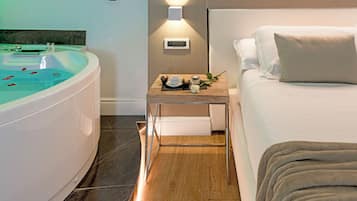 Una habitación de hotel moderna con una bañera grande, una mesita de noche con una taza y flores, y una cama bien hecha.