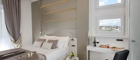 A modern hotel room with a bed, bedside table, and a desk with a view of the city.