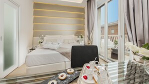 A modern hotel room with a large bed, a sitting area with a glass table, and a balcony with a view. - Vatican Style (Rome)