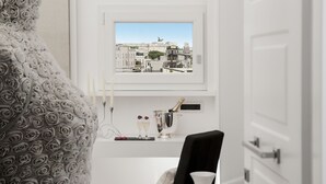 A room with a view of a cityscape through a window, a bed with a patterned headboard, a bedside table with a champagne bottle and glasses, and a black chair. - Vatican Style (Rome)