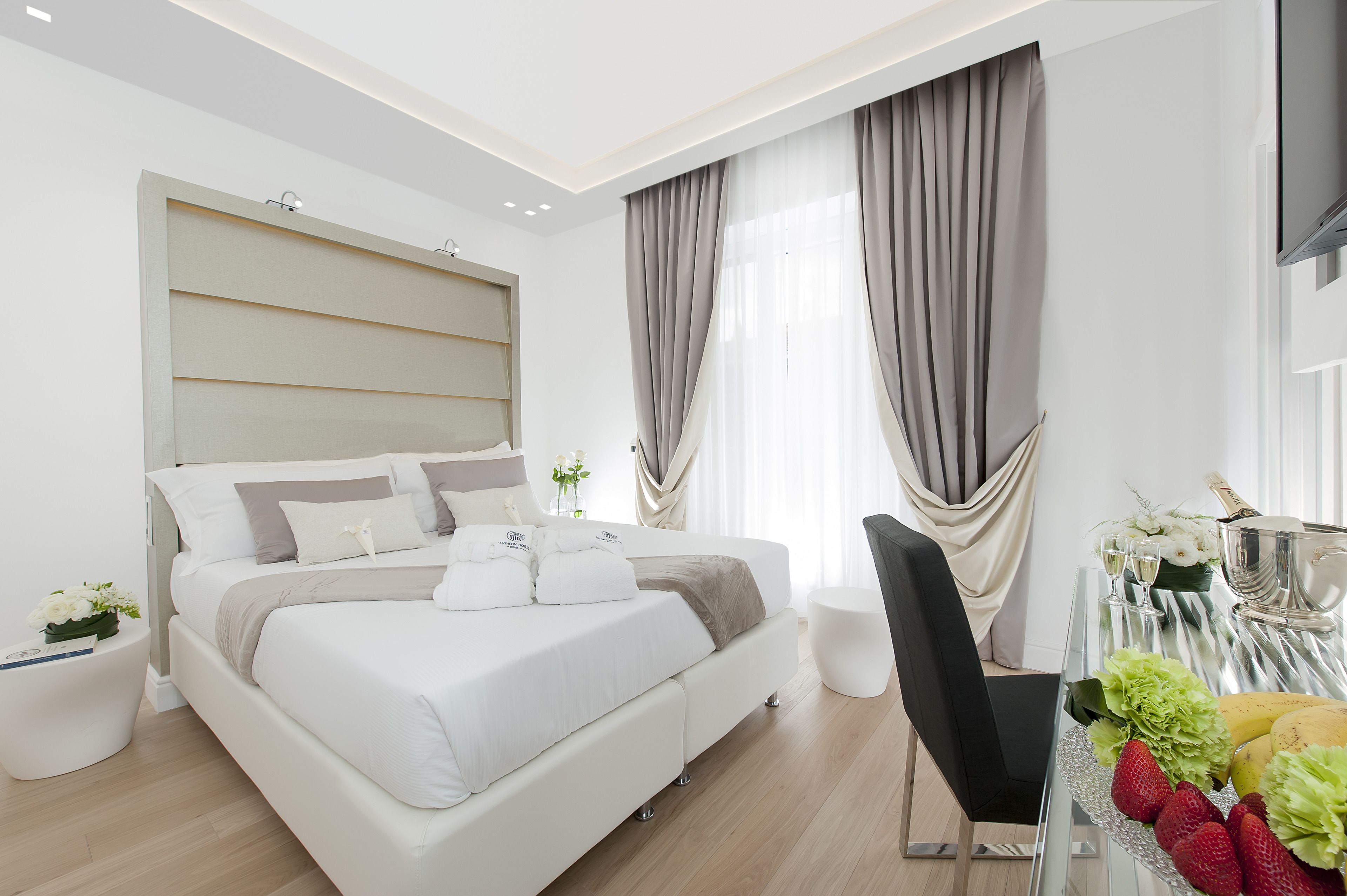Una habitación de hotel moderna con una cama grande, una mesa de vidrio con alimentos para el desayuno y un televisor montado en la pared.