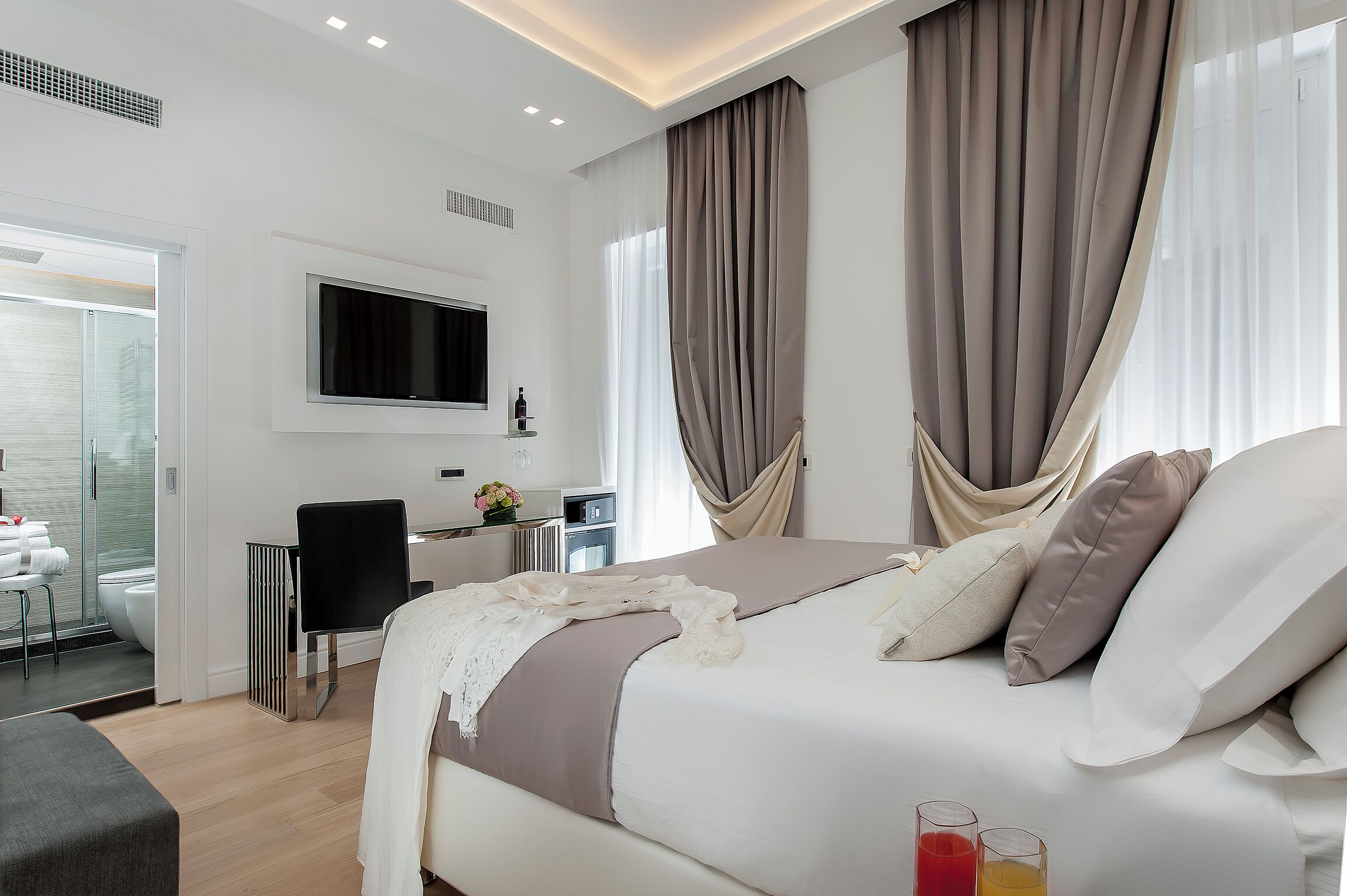A modern hotel room with a large bed, a TV mounted on the wall, and a desk with a chair.