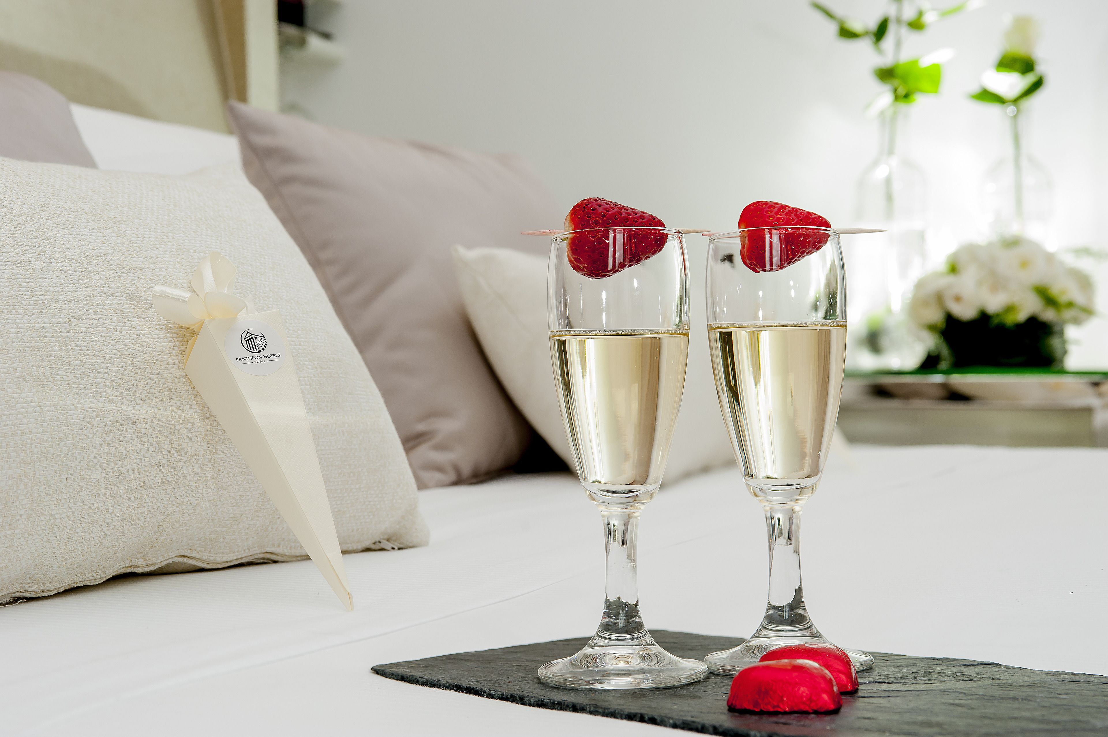 Two champagne glasses with strawberries on a bed with a pillow and a decorative item.