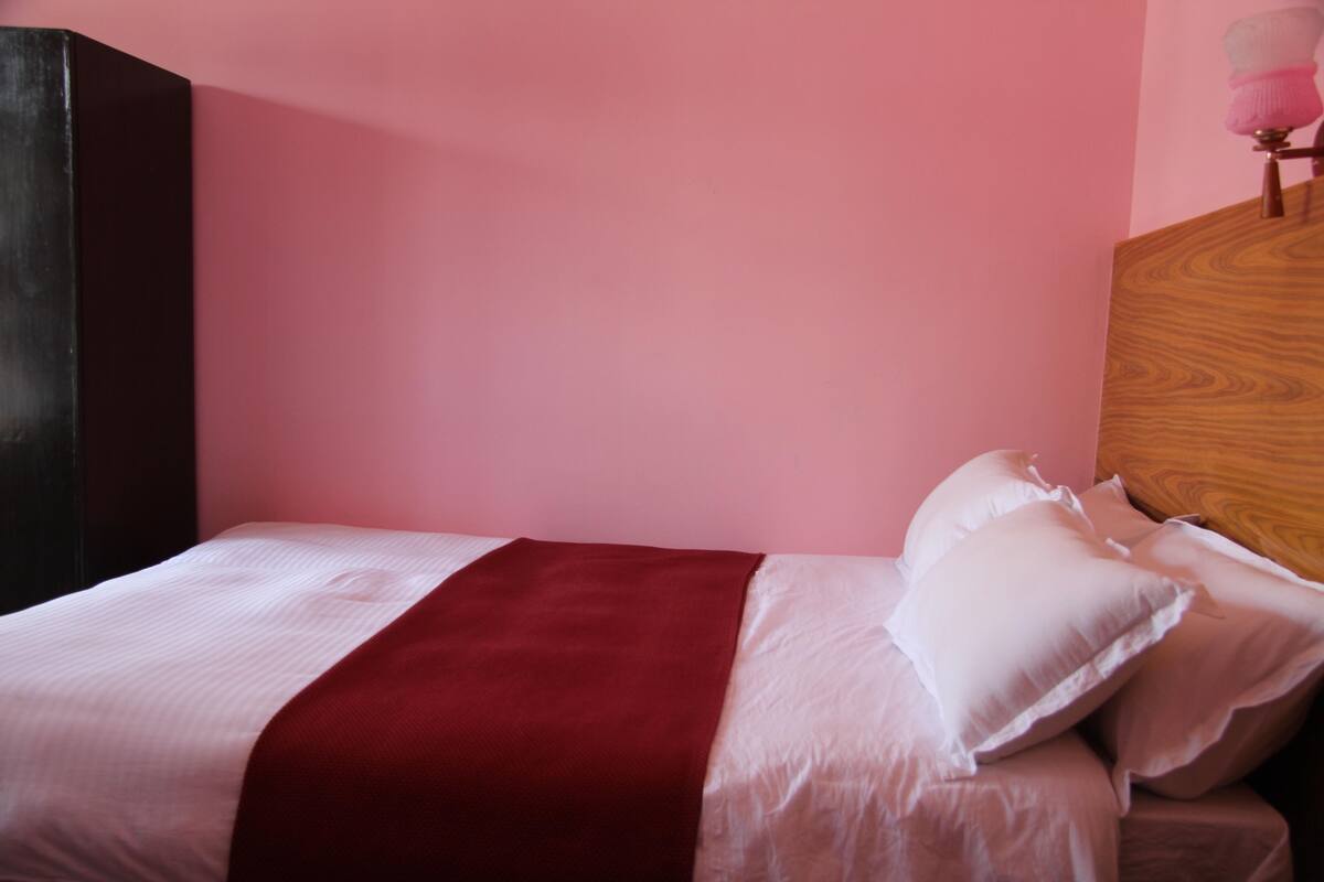 A bed with white and red bedding, a wooden headboard, and a pink wall.
