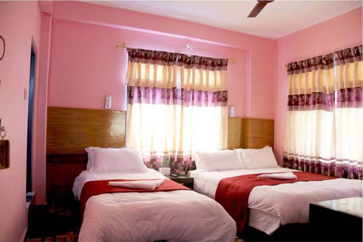 A hotel room with two beds, pink walls, and a wooden headboard.