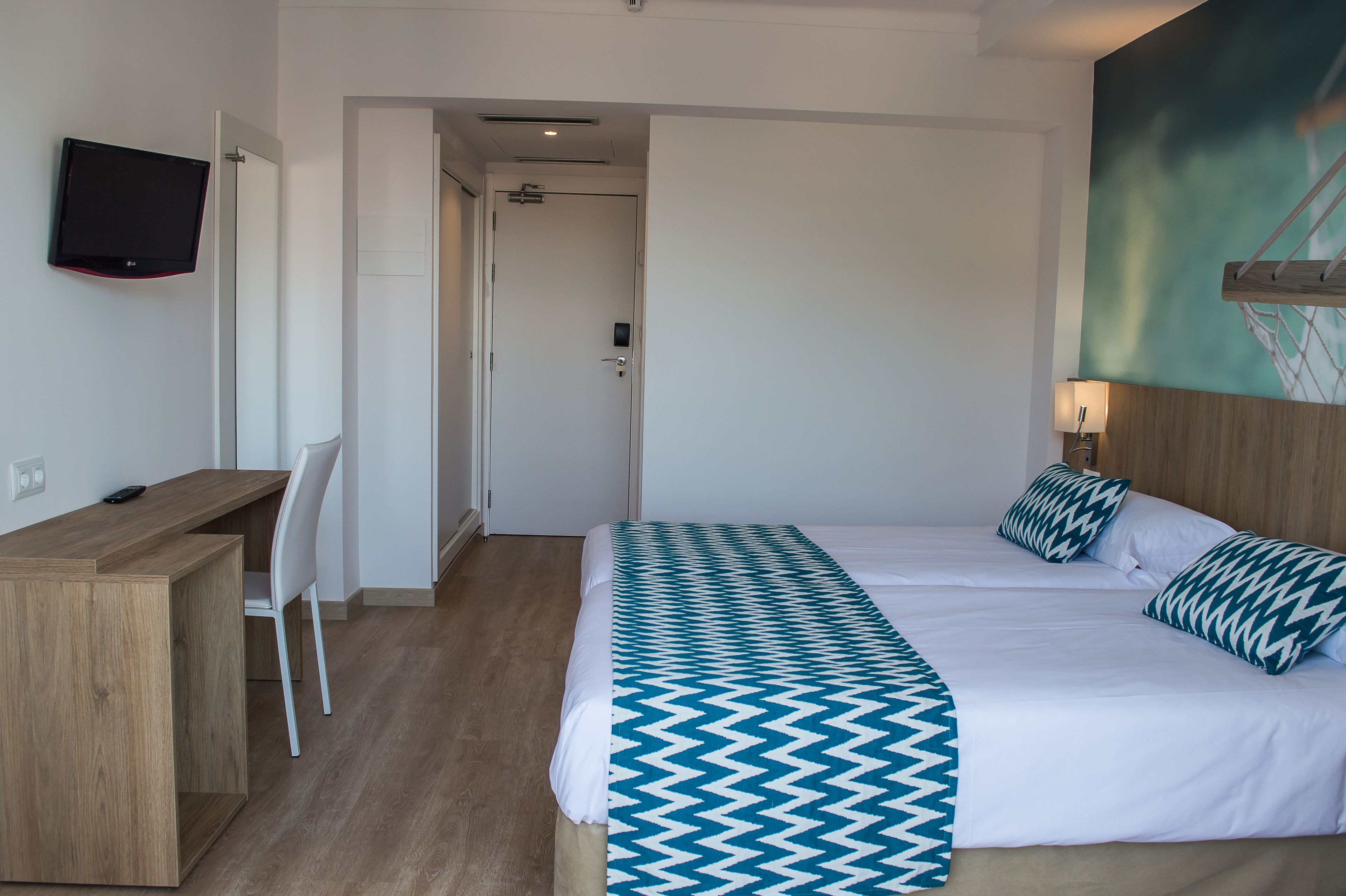Una habitación de hotel con una cama, un escritorio, una silla, un televisor y un cuadro en la pared.