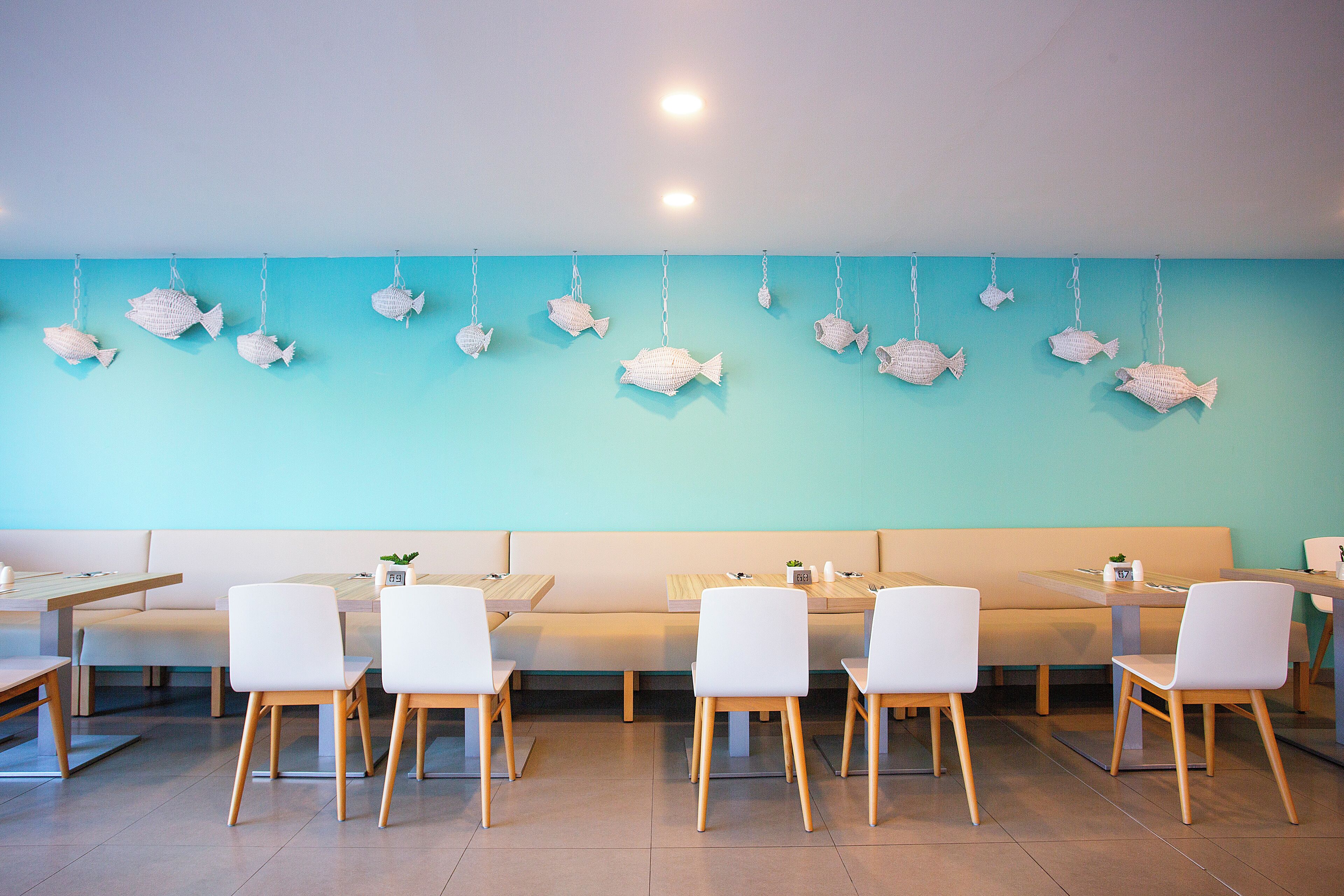 Ein Restaurant mit weißen Stühlen, einem langen Tisch und Fischdekorationen an der Wand.