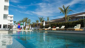 A swimming pool with lounge chairs and umbrellas, surrounded by palm trees and a white building. - BQ Sarah Hotel - Adults Only (Santa Margalida)