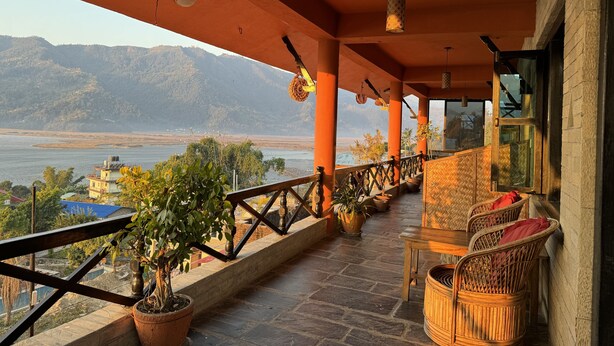 A balcony with a view of a river and mountains, wicker furniture, and potted plants. - Nar-Bis Hotel (Pokhara)