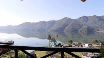 Vista de un lago con montañas al fondo y un edificio con balcón en primer plano.