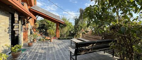 A courtyard with a stone patio, a wooden bench, and potted plants.