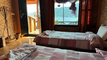A room with two beds, a wicker chair, a basket, and a view of a mountain and lake through a window.