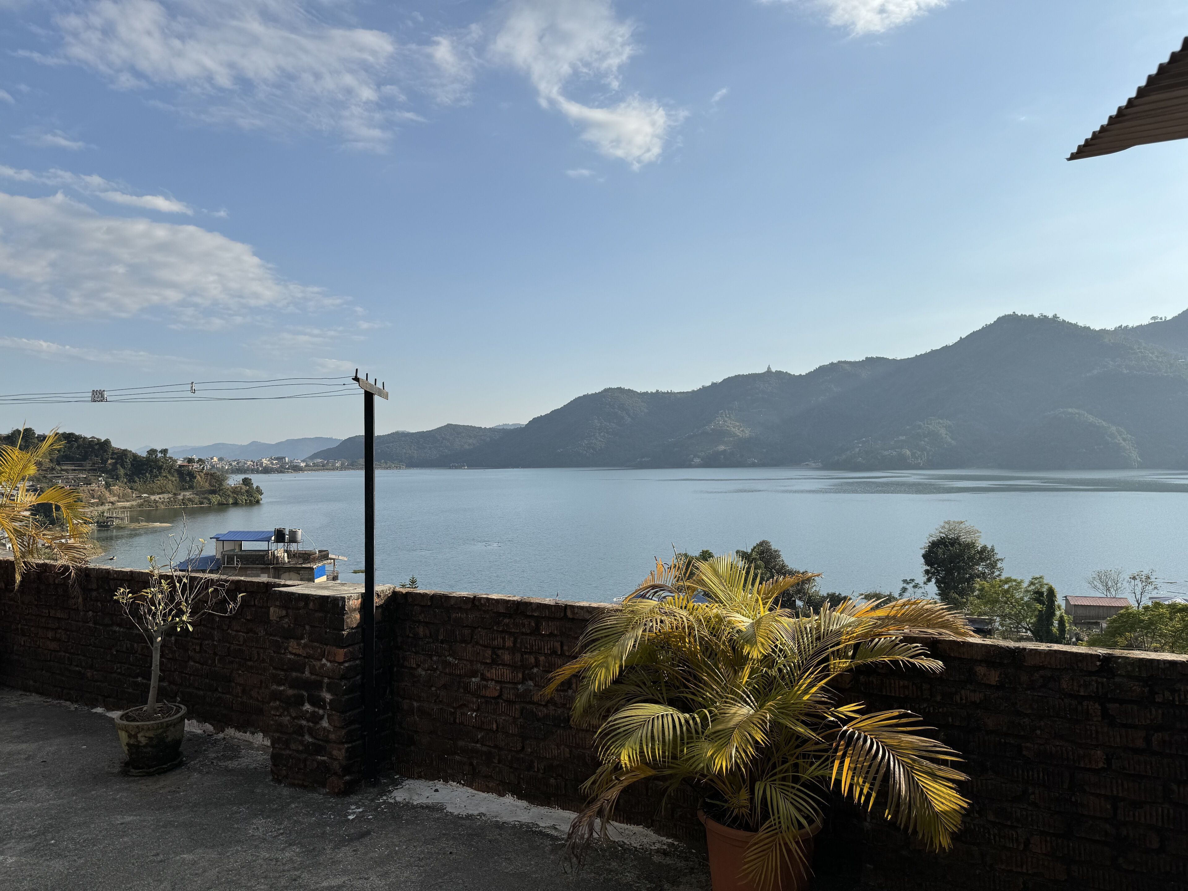 Une vue sur un lac, avec des montagnes en arrière-plan, un mur de briques et quelques plantes en pot.