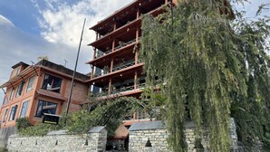 A multi-story hotel with a stone facade, balconies, and a large tree in front. - Nar-Bis Hotel (Pokhara)