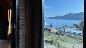 A room with a brick wall and a window overlooking a lake with buildings and mountains in the distance. - Nar-Bis Hotel (Pokhara)