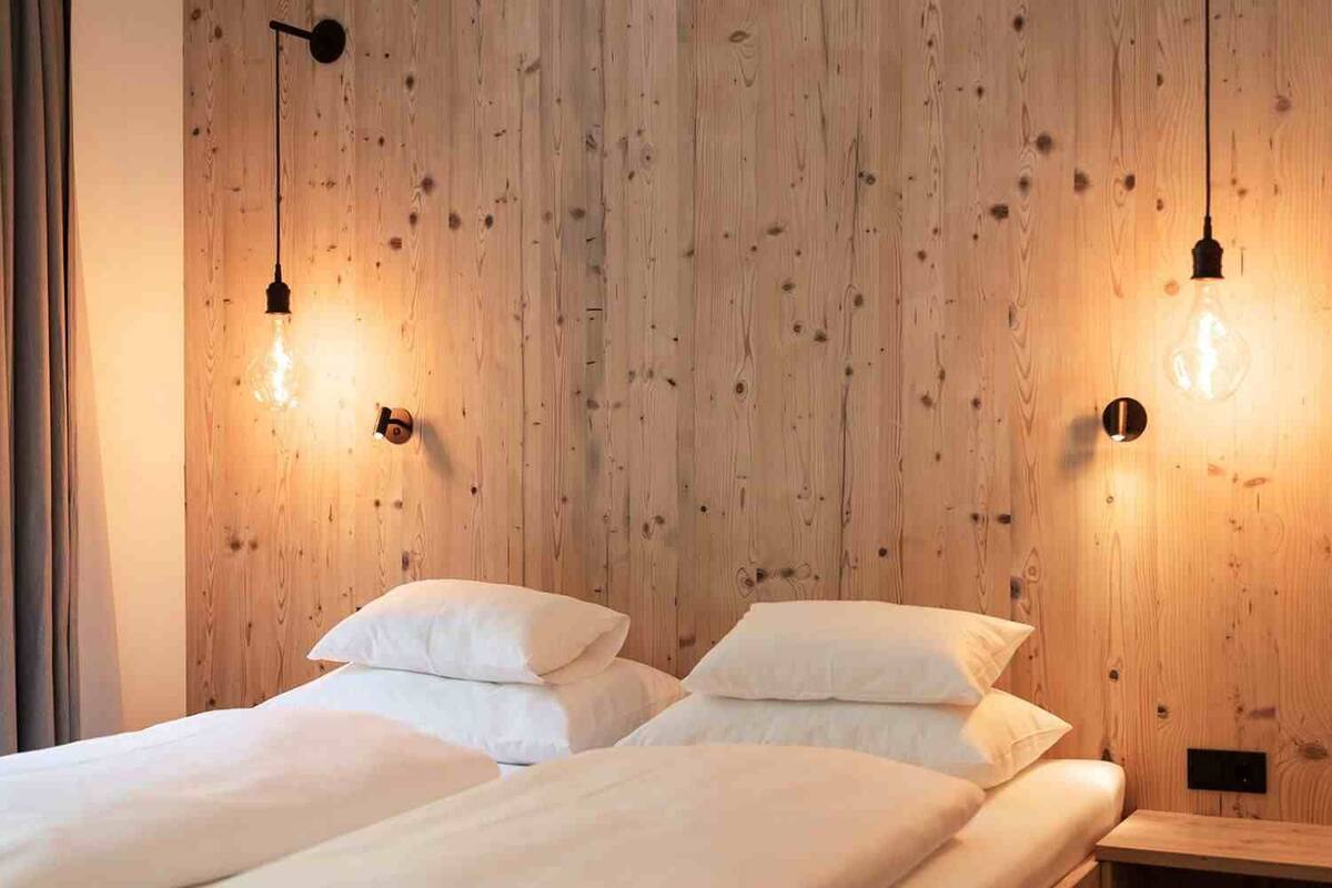Habitación con dos camas, paredes de madera e iluminación colgante.