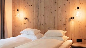 Habitación con dos camas, paredes de madera e iluminación colgante.