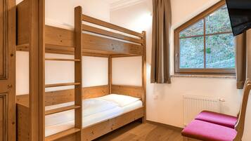 A bunk bed with a wooden frame and white bedding, a window with a view of trees, and a radiator on the wall.