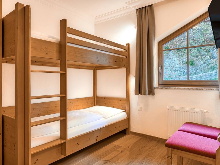 A bunk bed with a wooden frame and white bedding, a window with a view of trees, and a radiator on the wall.