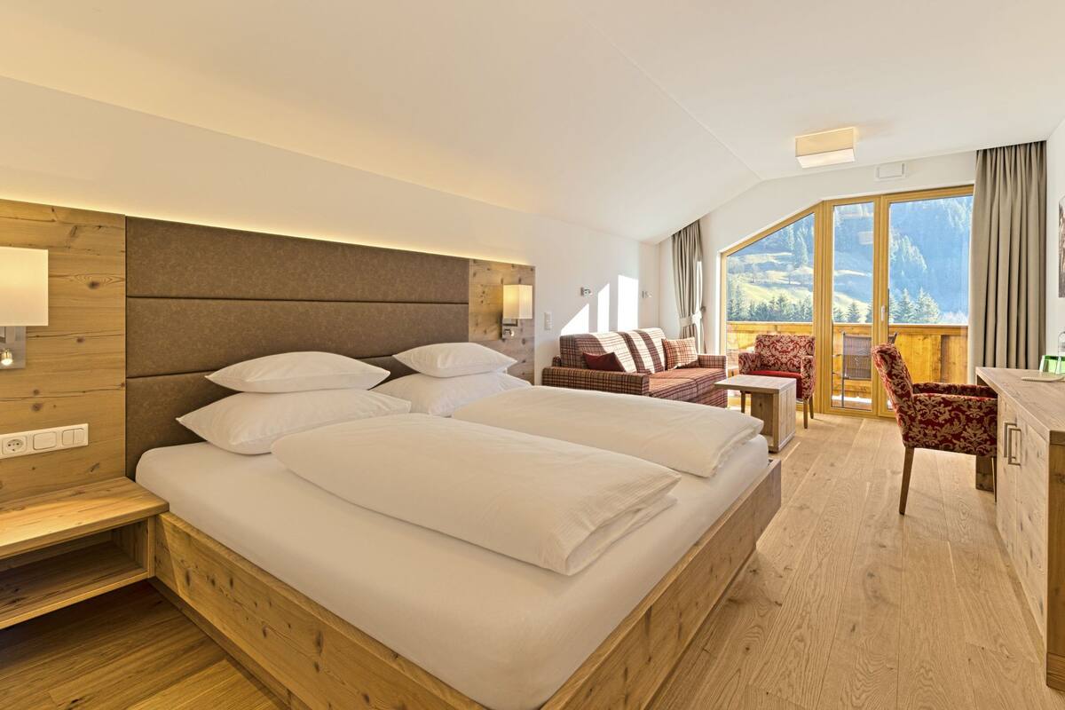 Habitación de hotel con una cama grande, un escritorio, una silla y un balcón con vistas a la montaña.