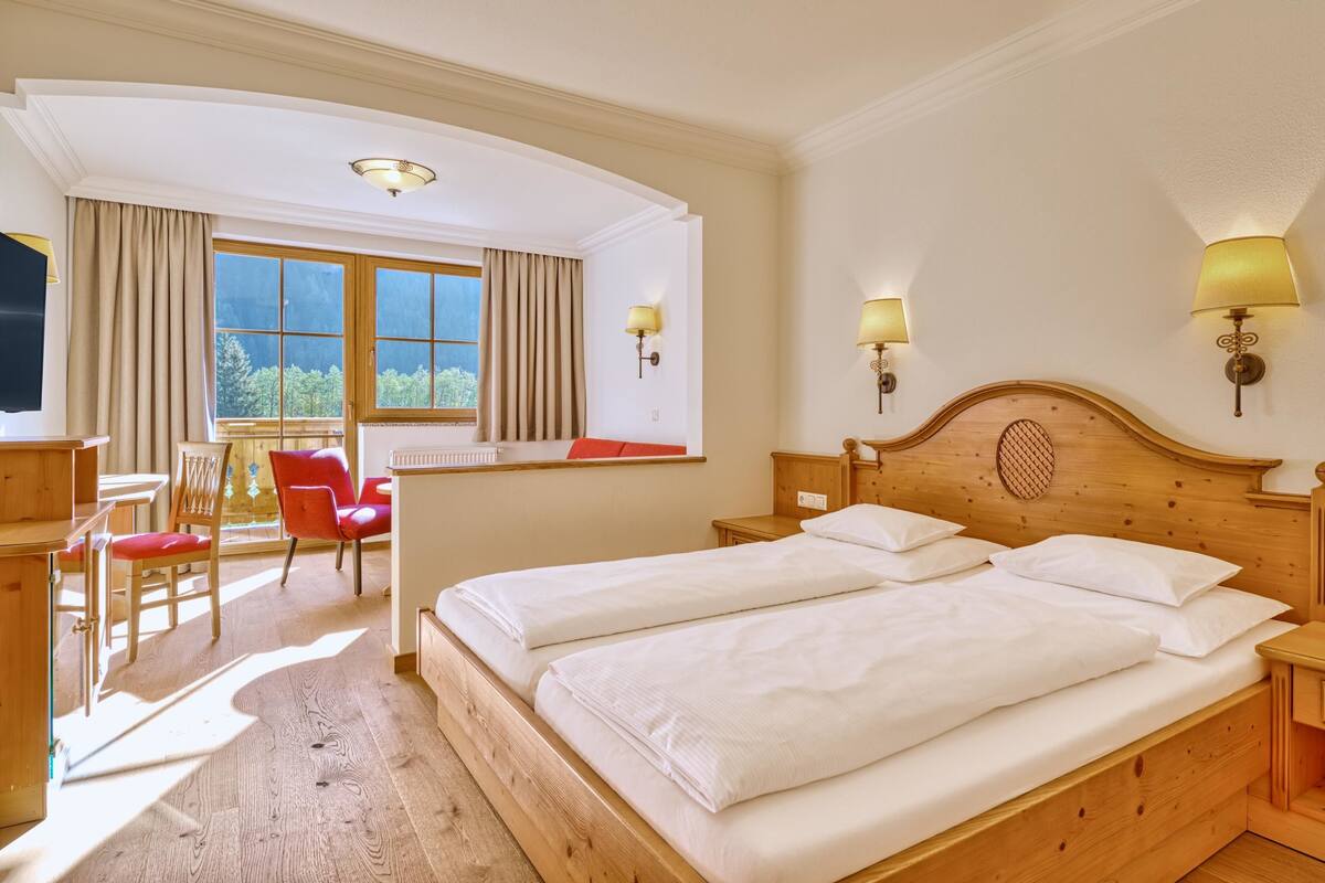 Habitación de hotel con dos camas, cabecero de madera, escritorio con silla, ventana con cortinas y lámparas fijadas a la pared.