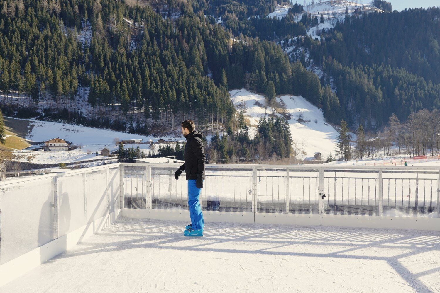 A person standing on a snow-covered slope with a view of a forested mountain range in the background.