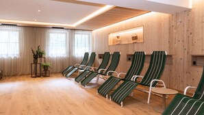 Una habitación con suelo de madera, sillones reclinables a rayas verdes, una mesita y una estantería adosada a la pared con objetos decorativos.