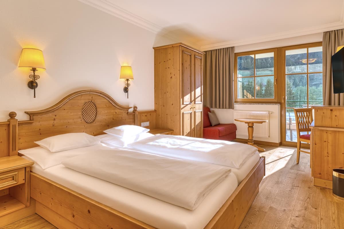 Una cama de madera con sábanas blancas, dos lámparas fijadas a la pared, una mesita y una silla.