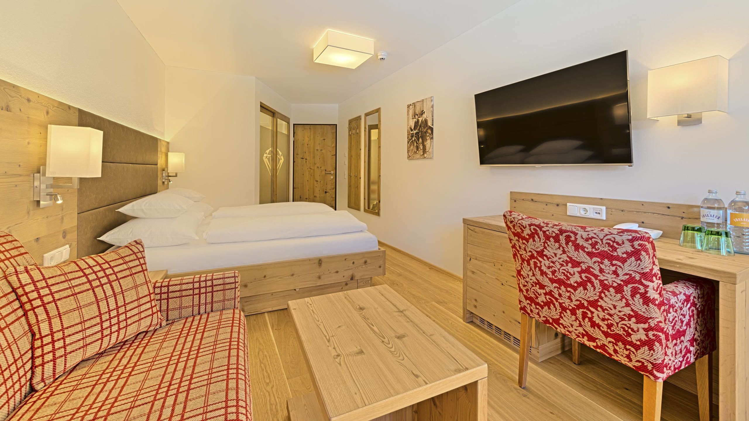 A hotel room with a bed, a desk with a chair, a TV, and a mirror.
