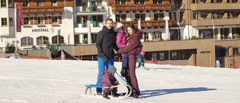A family on a sled in a snowy area with buildings labeled "KRISTALL" in the background.