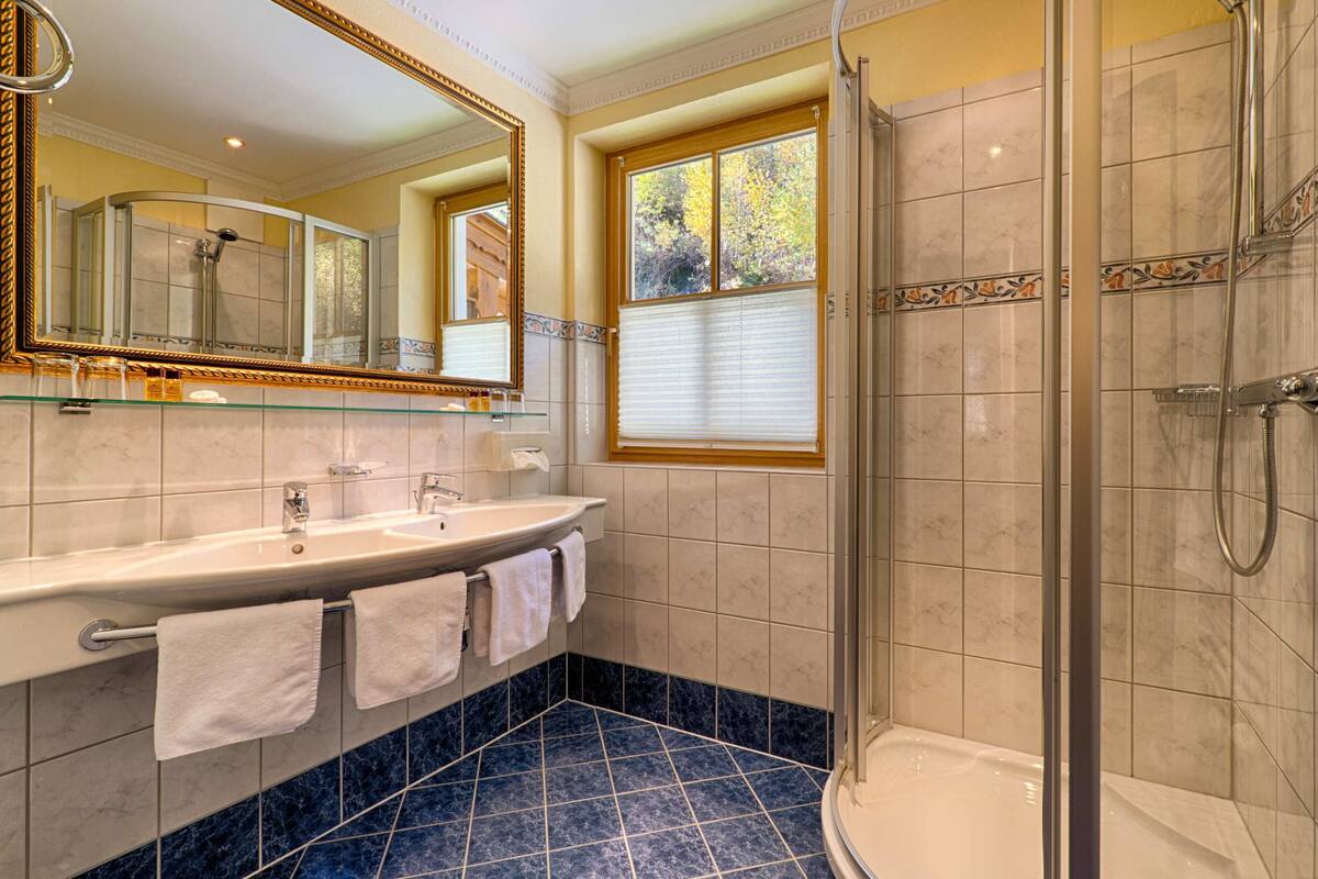 Un baño con un espejo grande, un lavamanos, una ducha y una ventana.