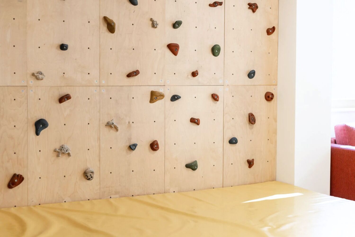 Un mur d'escalada amb diferents preses i una zona amb protecció de color groc a la base.