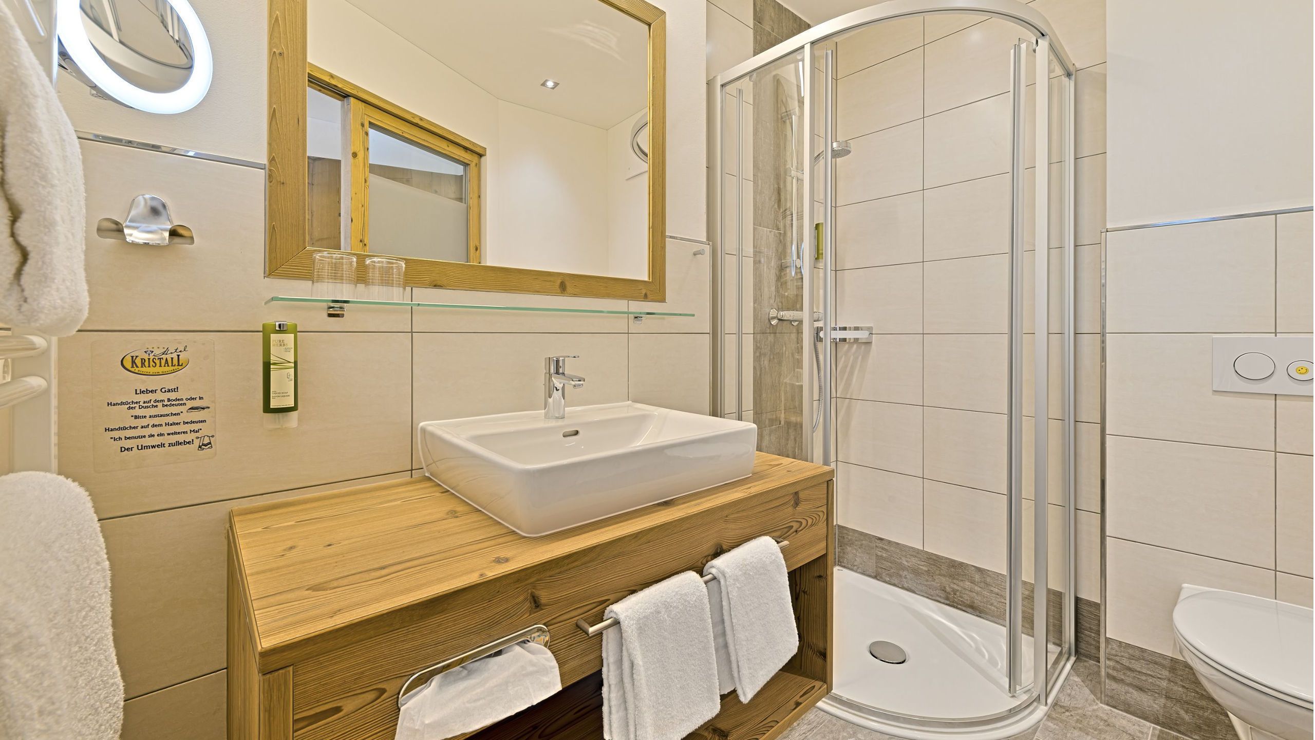 Un baño moderno con un espejo grande, un lavamanos, cabina de ducha de vidrio y tocador de madera.